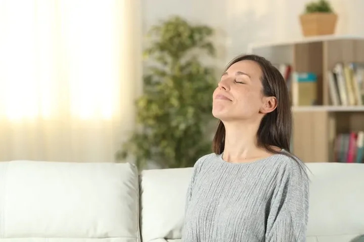 A woman sitting on a sofa with her eyes closed, breathing in the air of a freshly cleaned room